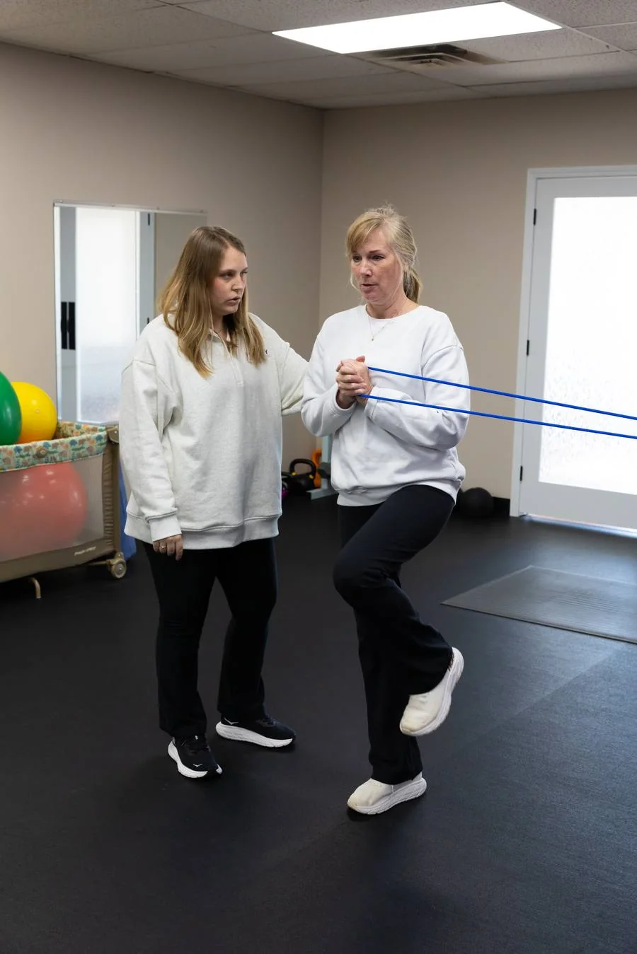 A pelvic health physical therapist guiding a patient through single-leg balance work with a resistance band